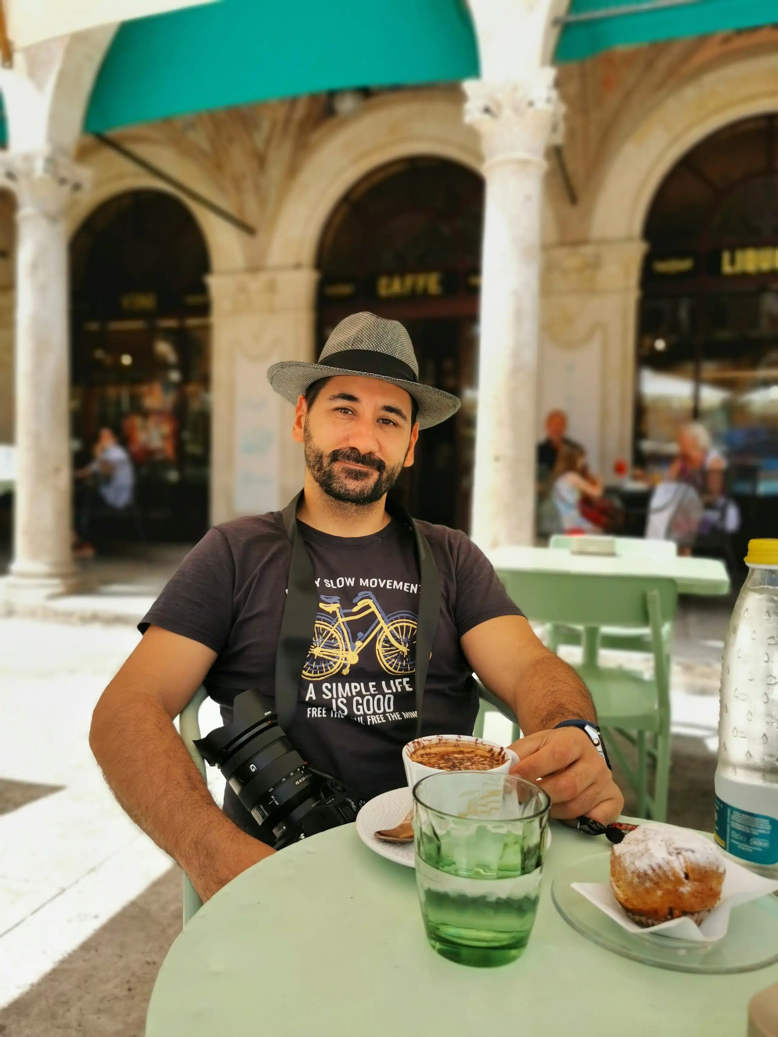 Photographer relaxing at an outdoor café with coffee and pastry.